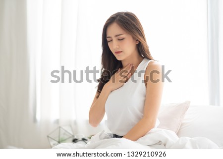 Asian Beautiful Woman in white pajamas suffering from Acid reflux while wake up on her bed in the morning. Illness, Disease, Symptom. Royalty-Free Stock Photo #1329210926