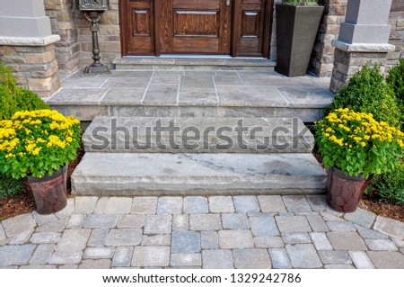 Flagstone applied to the original concrete veranda, natural stone steps, and paver walkway all provide a beautiful, fresh landscape update to this stately home. Royalty-Free Stock Photo #1329242786