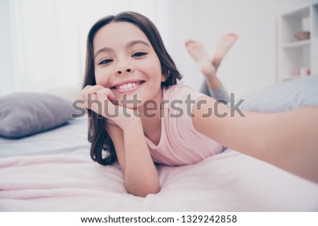 Close up photo cute sweet beautiful she her little girl crossed legs lying down homey sunday make take selfies speak skype wear home t-shirt pants comfortable apartments flat bright light colored room