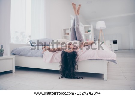 Full length body size photo funky beautiful she her little childish girl lying bed upside down show v-sign curly wavy playful wear home t-shirt pants comfortable flat bright light colored room indoors