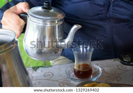 Pouring tea from tea pot to glass. Breakfast preparation concept. Traditional Turkish brewed tea drink in morning also as known in local language "Çay". Relaxing or resting mood, break time concept.