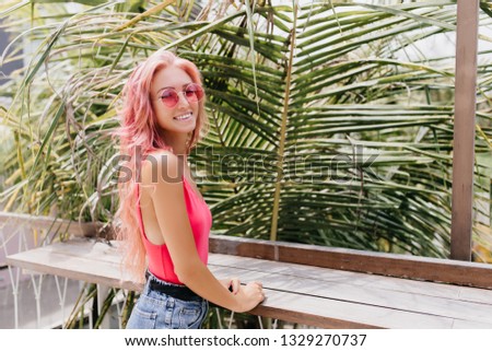 Pretty woman with wavy pink hair laughing to camera in summer day. Outdoor photo of amazing caucasian girl in trendy sunglasses posing with charming smile on nature background.