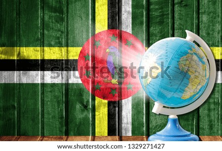 Globe with a world map on a wooden background with the image of the flag of Dominica. The concept of travel and leisure abroad.