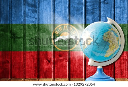 Globe with a world map on a wooden background with the image of the flag of Karachay Cherkessia. The concept of travel and leisure abroad.