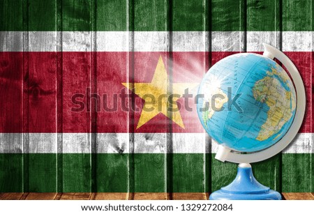 Globe with a world map on a wooden background with the image of the flag of Suriname. The concept of travel and leisure abroad.