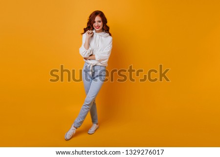Full-length portrait of attractive girl with ginger hair. Indoor shot of happy lady wears white sweater and jeans.