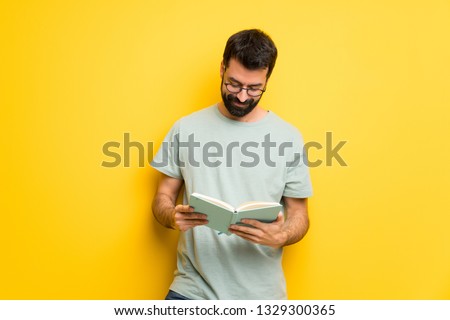 Man with beard and green shirt holding a book and enjoying reading