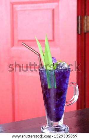 In selective focus Iced soft drinks of butterfly pea in a glass with a pandan leaf on top and blurred a red door background 