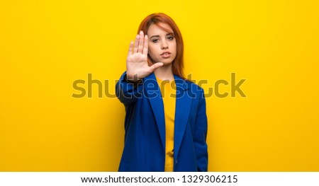 Young redhead woman with trench coat making stop gesture denying a situation that thinks wrong