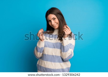 Young woman over blue wall making money gesture