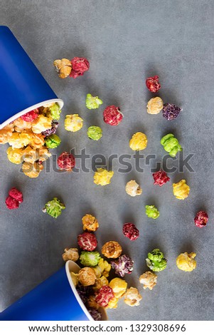 Bright multi-colored popcorn in blue paper cups on gray background. Soft focus.