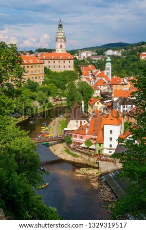 Cescy Krumlov historic center summer view. Cozy small European town with tiled red roofs. Vltava river, green trees, tile roof housesand Krumlov castle tower on the backgroung of blue cloudy sky.