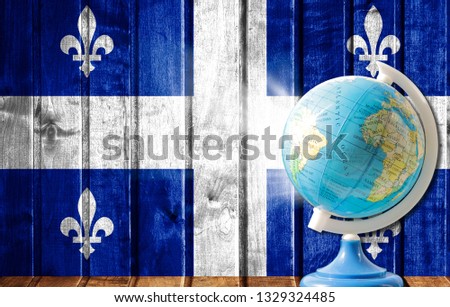 Globe with a world map on a wooden background with the image of the flag of Quebec. The concept of travel and leisure abroad.