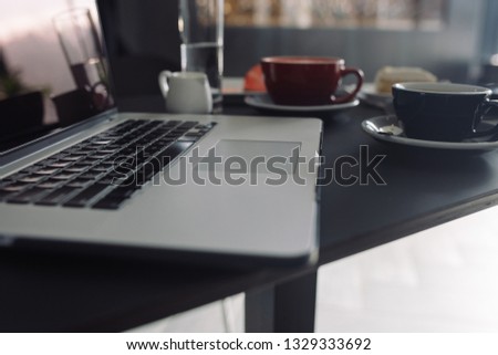 Close up of laptop keyboard, cups of coffee on background in coffee shop. Blogger workplace concept. 