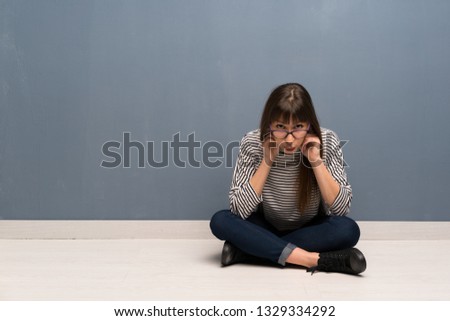 Woman with glasses sitting on the floor with glasses and surprised
