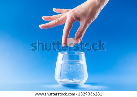 Headache medicine. Woman hand puts aspirin into glass with water. Health care concept with blue background.
