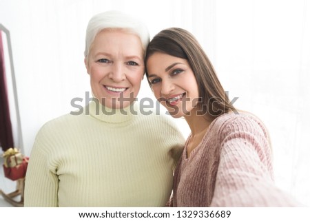 Senior mother and daughter taking selfie, having fun at home