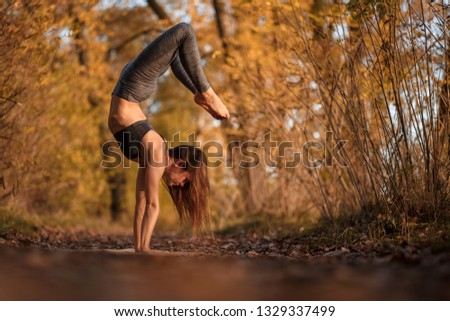 Young woman practicing yoga exercise in autumn park with yellow leaves. Sports and recreation lifestyle.