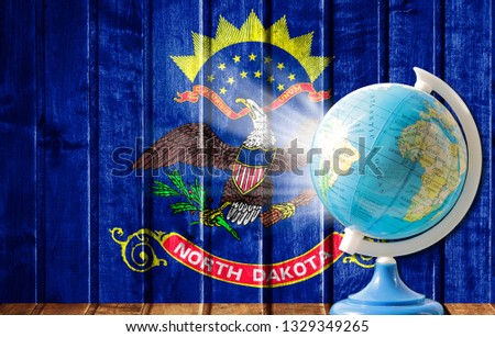 Globe with a world map on a wooden background with the image of the flag State of North Dakota. The concept of travel and leisure abroad.