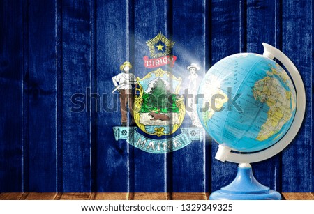 Globe with a world map on a wooden background with the image of the flag State of Maine. The concept of travel and leisure abroad.