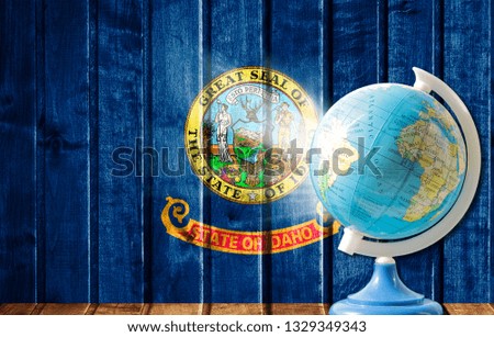 Globe with a world map on a wooden background with the image of the flag State of Idaho. The concept of travel and leisure abroad.