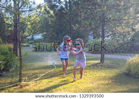 Child playing with garden sprinkler. Kids run and jump. Summer outdoor water fun in the backyard. Children play with hose watering flowers. Kids splash on sunny day