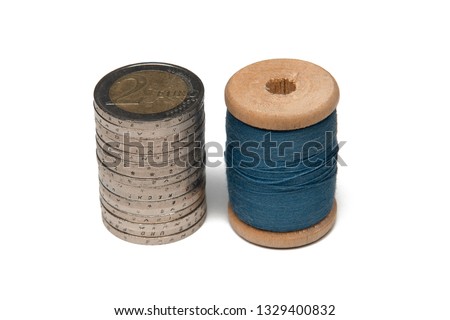 Rows of coins isolated on white background next to multicolored thread on wooden spool