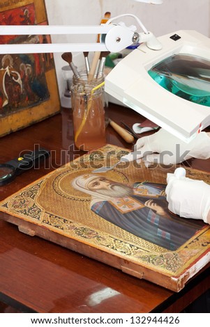 Closeup of accurate restoration of old icon with  filling knife at workshop