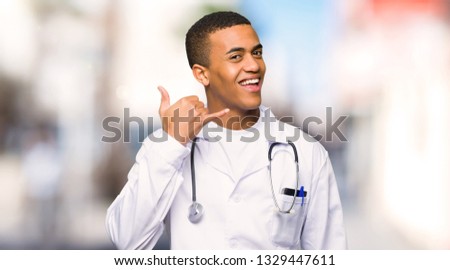 Young afro american man doctor making phone gesture. Call me back sign at outdoors