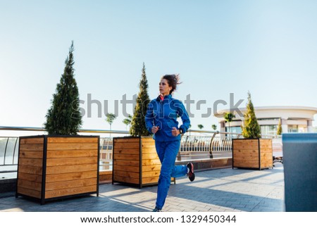Young woman wearing sweat suit jogging on empty city street in the morning Royalty-Free Stock Photo #1329450344