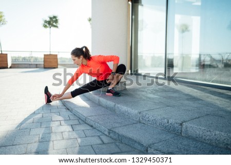 Young woman wearing long sleeve t-shirt listening music while stretching before jogging exercise