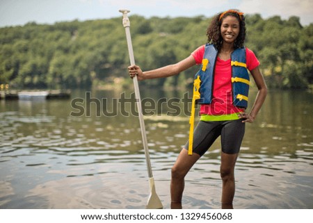 Portrait of a smiling young woman holding paddleboard oar.
