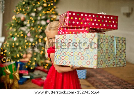 Young girl carrying a stack of Christmas presents.