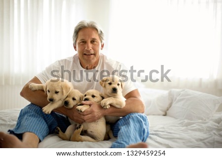 Middle aged man holding Labrador puppies while sitting on his bed.