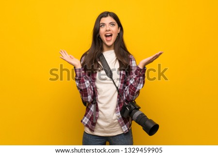 Photographer teenager girl over yellow wall with shocked facial expression