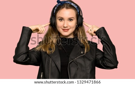 Teenager girl with leather jacket listening to music with headphones on isolated pink background