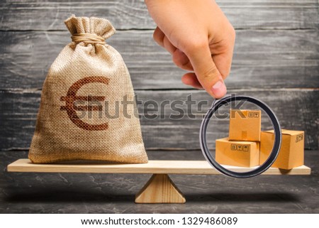 Magnifying glass is looking at a bag of euro money and a bunch of boxes on the scales. Economic relations between subjects, the global economic model. trade balance between countries, exchange Royalty-Free Stock Photo #1329486089
