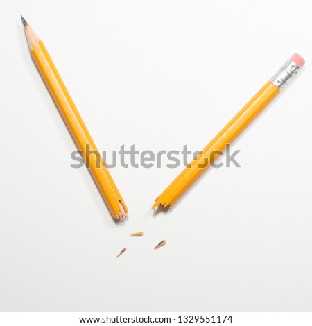 A broken pencil lying on plain white paper at an acute angle with fragments scattered in between Royalty-Free Stock Photo #1329551174
