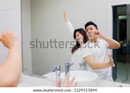 Image of cheerful Asian couple brushing teeth in the bathroom while dancing front a mirror