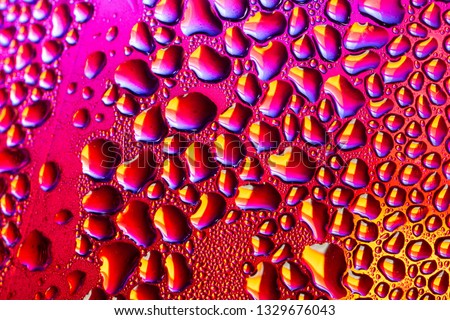 A close-up of droplets of water, rain or condensation on a sheet of transparent material beyond can be seen bright coloured neon colours such as a city street after the rain

