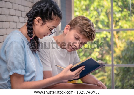 Caucasian teenage boy and Asian teenage girl reading book together