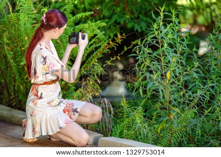 Red haired young woman taking a photo of a pond in botanical gardens with a digital camera