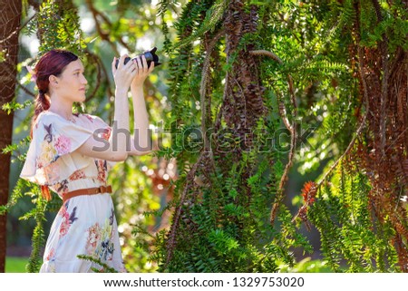 Beautiful woman taking a photo of foliage in a botanical garden with a digital camera