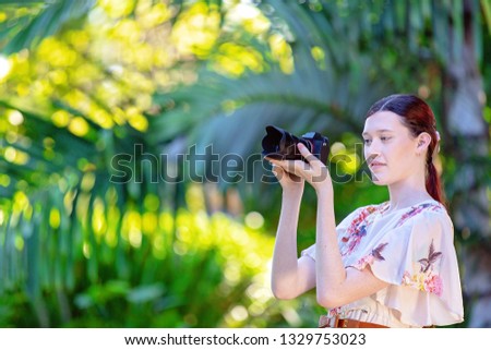 Beautiful young woman focusing her digital camera to take a photo in a colorful garden