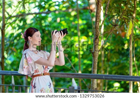Pretty woman focusing her digital camera to take a photo in a colorful garden with forest foliage