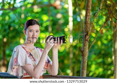 Beautiful young woman holding a digital camera read to take a photo in a colorful garden background