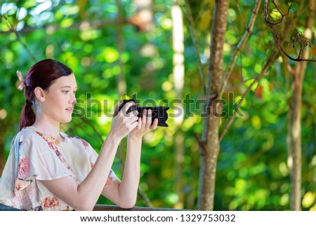 Pretty woman focusing her digital camera to take a photo in a colorful garden with forest foliage