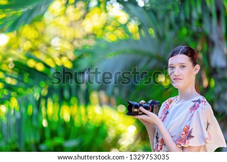 Beautiful young woman holding a digital camera in a colorful green and yellow garden backdrop
