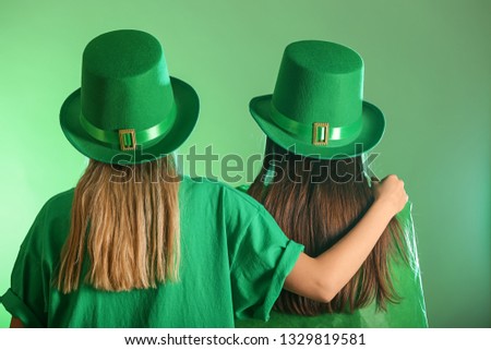 Young women in green hats on color background. St. Patrick's Day celebration