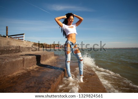 Silhouette of a young beauty sporty woman in a short tank top and blue ripped jeans posing against the sea and pier,   close up. Summer concept. Holiday travel.